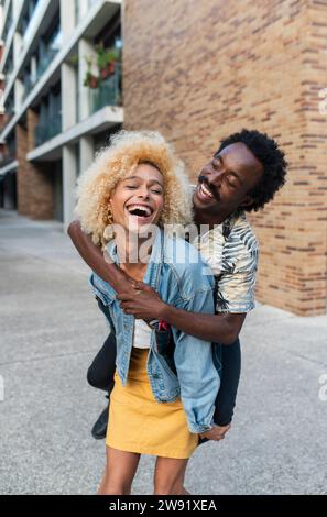 Heureuse femme transgenre piggybacking petit ami devant le bâtiment Banque D'Images