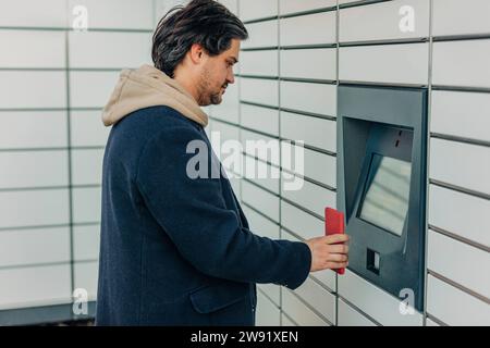 Homme scannant le code QR avec le téléphone intelligent sur la machine de casier à colis Banque D'Images