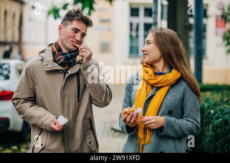 Couple souriant mangeant des hamburgers debout dans la rue Banque D'Images