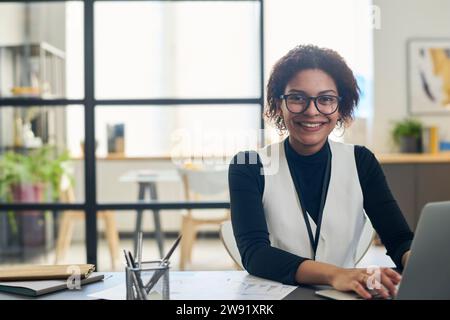 Heureuse jeune femme d'affaires assise avec ordinateur portable au bureau Banque D'Images