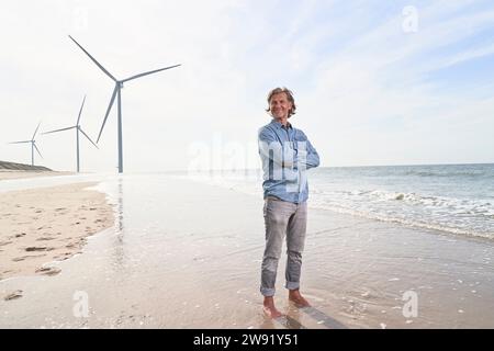 Heureux homme d'affaires senior debout devant les éoliennes à la plage Banque D'Images