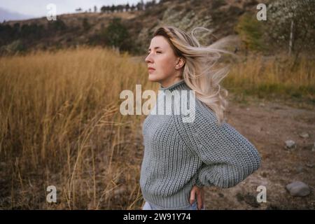 Femme blonde portant un pull tricoté debout près de hautes herbes sèches Banque D'Images