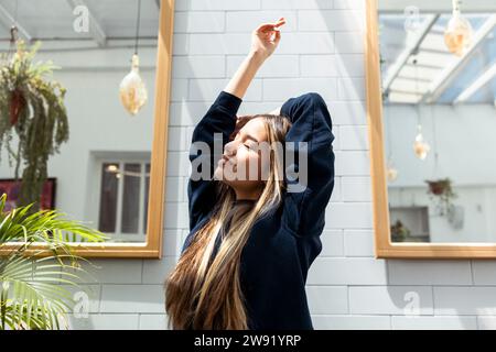 Jeune femme avec les yeux fermés étirant les bras devant le mur à la maison Banque D'Images
