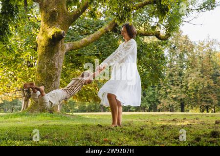 Femme joueuse filant son fils sur l'herbe au parc Banque D'Images