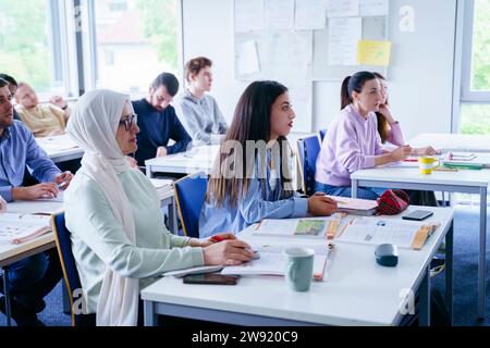 Amis multi-ethniques assis à des bureaux assistant à des conférences dans la salle de classe Banque D'Images