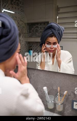 Femme appliquant des caches oculaires devant le miroir à la maison Banque D'Images