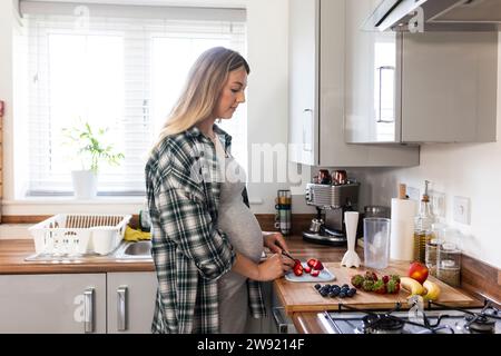 Femme enceinte coupant des fraises dans la cuisine à la maison Banque D'Images