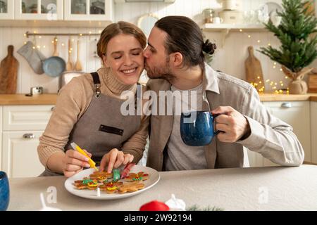 Homme embrassant femme décorant des biscuits à table Banque D'Images