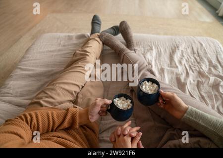 Couple tenant des tasses de chocolat chaud avec des guimauves sur le lit à la maison Banque D'Images