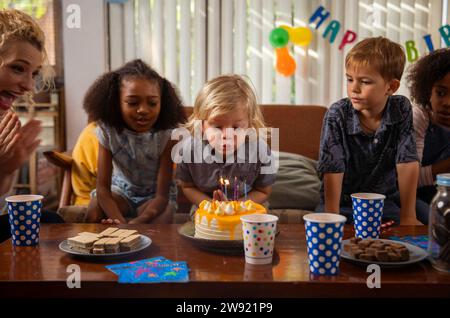 Garçon soufflant des bougies sur son gâteau d'anniversaire avec des amis regardant Banque D'Images