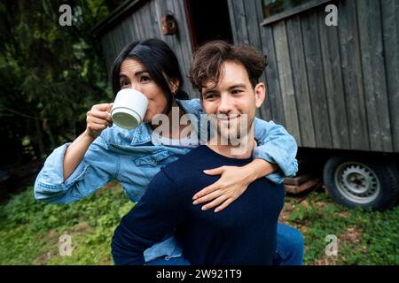 Jeune homme souriant donnant un tour de gigyback à la femme buvant du café Banque D'Images