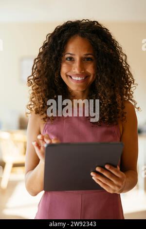 Femme d'affaires souriante avec les cheveux bouclés tenant la tablette PC Banque D'Images