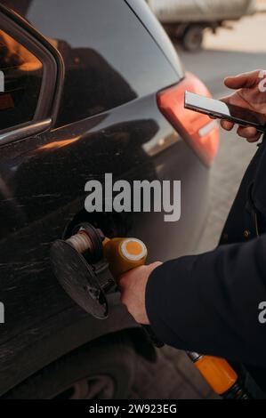Homme ravitaillant la voiture et tenant le téléphone intelligent en main Banque D'Images