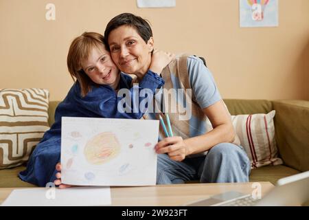 Mère souriante et sa fille avec le syndrome de Down montrant le dessin Banque D'Images