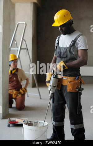 Ouvrier de construction mélangeant du ciment avec un outil dans un seau sur le site Banque D'Images