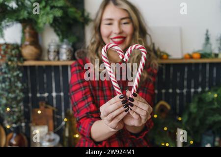 Femme souriante faisant forme de coeur avec des cannes de bonbons à la maison Banque D'Images