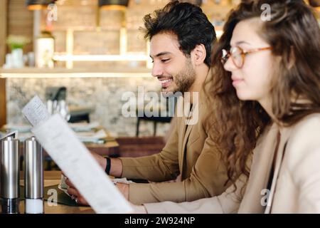 Jeunes collègues souriants lisant le menu au restaurant Banque D'Images