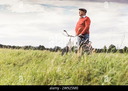 Homme senior debout à vélo et regardant la vue dans le champ Banque D'Images