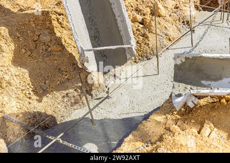 Le travailleur de la construction verse le béton de ciment dans les tranchées pour former la fondation de la maison Banque D'Images