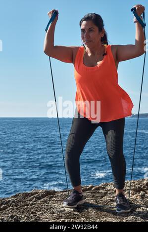 Femme latine, d'âge moyen, portant des vêtements de sport, s'entraînant, faisant des exercices physiques, musculature, avec bande élastique, brûler des calories, garder la forme Banque D'Images