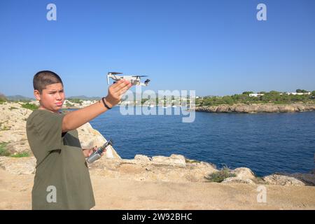 Heureux adolescent garçon, préparant et finalisant les détails du vol de drone, concept technologique Espagne, Îles Baléares Banque D'Images