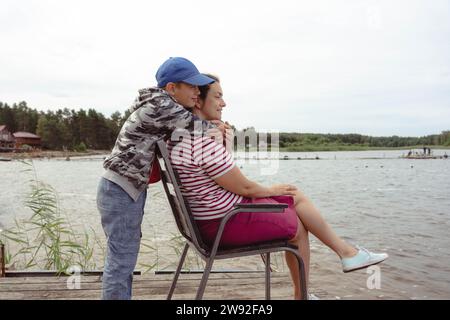 Un moment réconfortant capturé alors qu'un fils embrasse amoureusement sa mère lors d'un voyage de camping familial au bord du lac, symbolisant le lien et l'affection avec Banque D'Images