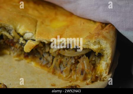 Un reste de tarte maison avec une pâte fine et une garniture de légumes composée de chou, de morceaux de champignons et d'oignons debout dans une cuisine élégante. Banque D'Images