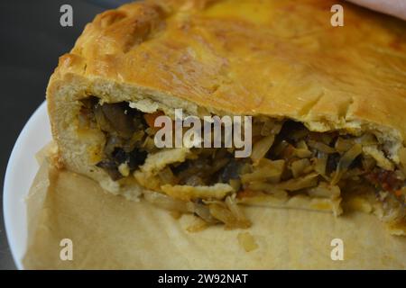 Un reste de tarte maison avec une pâte fine et une garniture de légumes composée de chou, de morceaux de champignons et d'oignons debout dans une cuisine élégante. Banque D'Images