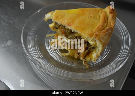 Un morceau de tarte maison coupé avec une pâte fine et une garniture de légumes composée de chou, de morceaux de champignons et d'oignons placés sur un verre, transparent Banque D'Images