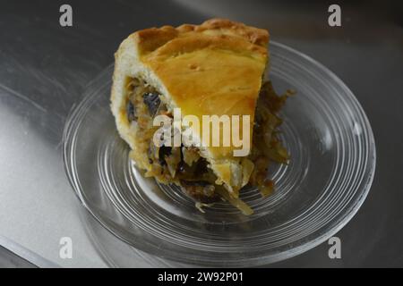 Un morceau de tarte maison coupé avec une pâte fine et une garniture de légumes composée de chou, de morceaux de champignons et d'oignons placés sur un verre, transparent Banque D'Images