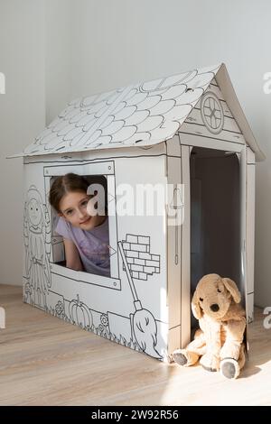 Une fille joue avec une maison de poupée. Jouet mou pour chien. Un chien est l'ami d'une personne. Un enfant joue à la maison avec son chien en peluche. Banque D'Images