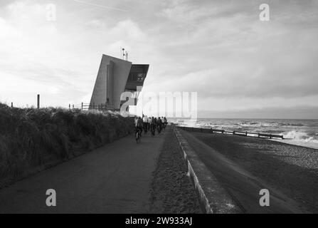 Un groupe de cyclistes court le long de la promenade extérieure, devant la tour d'observation de Rossall point, Fleetwood, Lancashire, Royaume-Uni, Europe Banque D'Images