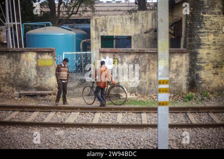 Deux hommes indiens portant des chandails et debout à côté des voies ferrées au Bengale. On a un cycle pour le transport et le parking, la vie urbaine en Inde Banque D'Images