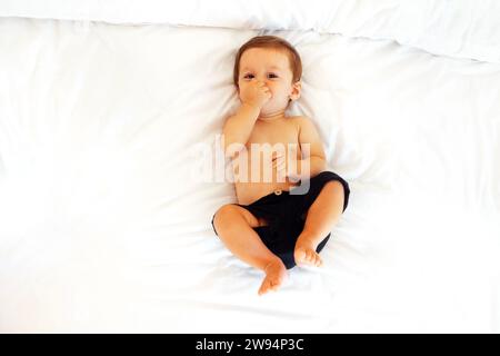 Le bébé mignon rit et allongé sur un drap blanc sur le canapé. Un petit garçon sourit sur le lit à la maison. Sweet Happy bambin s'amuse. Vue Banque D'Images