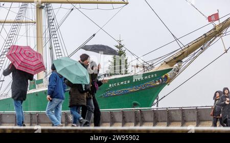 Hambourg, Allemagne. 24 décembre 2023. Les marcheurs passent devant le navire du musée Rickmer Rickmers sur l'Elbe dans la bruine. La tempête s'est affaiblie, mais beaucoup de pluie et de neige sont attendues dans certaines régions d'Allemagne ce week-end. Les niveaux d'eau de nombreuses rivières augmenteront également. Les voyageurs ferroviaires doivent être prêts pour les trains complets. Crédit : Markus Scholz/dpa/Alamy Live News Banque D'Images