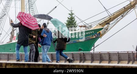 Hambourg, Allemagne. 24 décembre 2023. Les marcheurs passent devant le navire du musée Rickmer Rickmers sur l'Elbe dans la bruine. La tempête s'est affaiblie, mais beaucoup de pluie et de neige sont attendues dans certaines régions d'Allemagne ce week-end. Les niveaux d'eau de nombreuses rivières augmenteront également. Les voyageurs ferroviaires doivent être prêts pour les trains complets. Crédit : Markus Scholz/dpa/Alamy Live News Banque D'Images