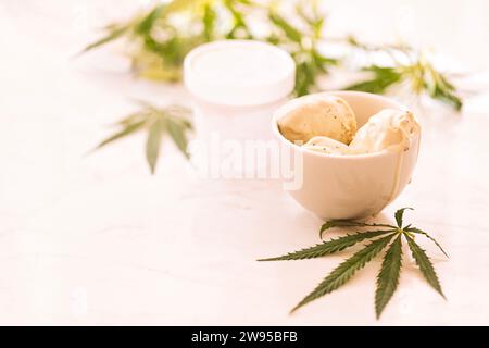 Une feuille de chanvre repose sur une maquette de bocaux de crème glacée sur une table en marbre blanc. Feuilles de cannabis vert sur le fond. Alimentation biologique et santé. Banque D'Images