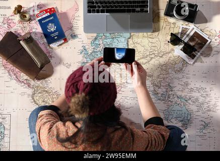 Une femme assise sur une carte et se préparant pour un voyage avec des accessoires de voyage Banque D'Images