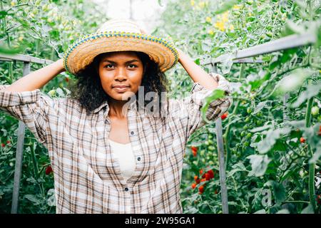 Une agricultrice souriante se tient parmi les plants de tomates dans une serre représentant le bonheur et les soins pour Banque D'Images