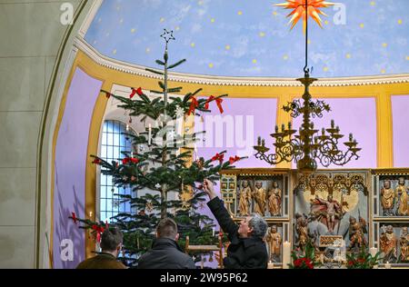 Sieversdorf, Allemagne. 24 décembre 2023. Frank Schütte (r), lector, allume les bougies sur le sapin de Noël au début des Vêpres de Noël dans l'église protestante du village le jour de Noël. La veille de Noël, plusieurs services sont offerts dans presque toutes les églises protestantes. Dans la petite église du village de Sieversdorf, des Vêpres de Noël avec une pièce de nativité ont lieu chaque après-midi de Noël. Des chants bien connus sont chantés et des prières sont dites. Des enfants et des jeunes des villages environnants jouent le jeu de la nativité. Crédit : Patrick Pleul/dpa/Alamy Live News Banque D'Images