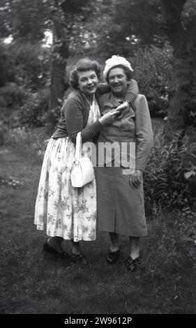 Années 1950, historique, ma mam.... debout à l'extérieur, une jeune femme portant une longue robe à motifs de fleurs donnant à sa mère un câlin affectueux, Angleterre, Royaume-Uni. Banque D'Images