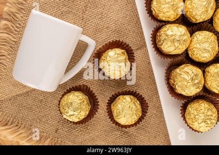 Plusieurs chocolats avec soucoupe en céramique blanche, tasse sur serviette en jute, macro, vue de dessus. Banque D'Images