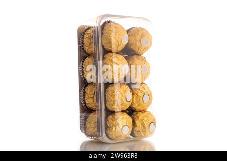 Plusieurs bonbons au chocolat avec des noix dans un emballage en papier dans une boîte en plastique, macro, isolé sur un fond blanc. Banque D'Images