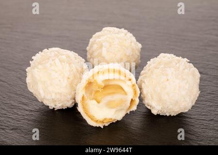 Un demi-bonbon avec des flocons de noix et de noix de coco et trois bonbons entiers sur pierre d'ardoise, macro. Banque D'Images