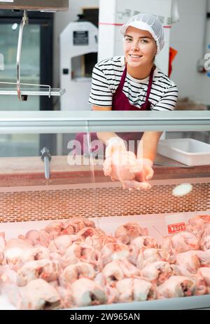 Jeune fille se tient derrière le comptoir dans le département de viande du supermarché et montre la carcasse de poulet Banque D'Images