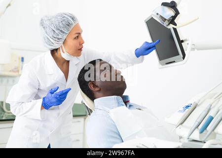 Femme dentiste pointant sur l'écran pour montrer des informations au patient Banque D'Images