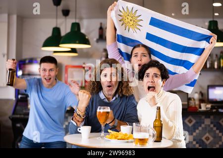 Les fans du drapeau de l'Uruguay célèbrent la victoire de leur équipe préférée au bar à bière Banque D'Images