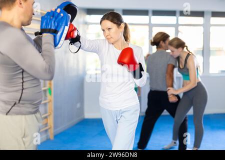 Femme travaille sur la force et la vitesse des mitaines de punch de boxe avec l'aide du partenaire masculin dans les pattes de boxe. L'homme joue le rôle de cible et mannequins pendant t Banque D'Images