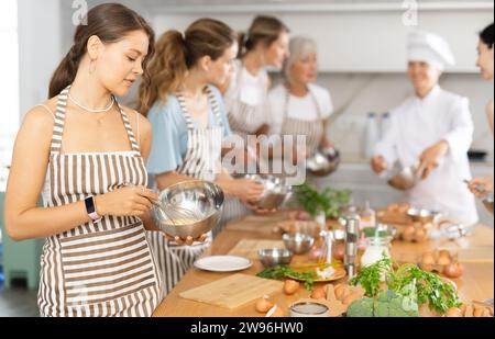 Jeune femme en tablier apprenant à cuisiner à la classe de maître de cuisine Banque D'Images