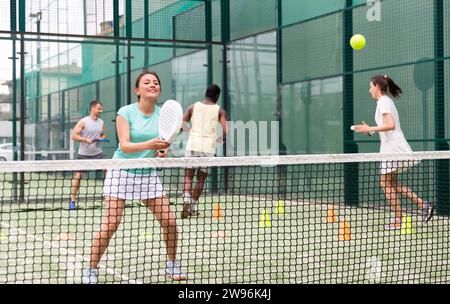 Portrait d'une femme joyeuse joueuse de paddle-tennis exécutant la technique des coups à l'entraînement de groupe au court Banque D'Images